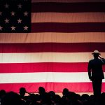 A solemn moment as a soldier salutes the American flag during a ceremony inside an auditorium.